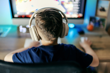 Young boy wearing headphones concentrating on the computer screen, actively engaged in online gaming.